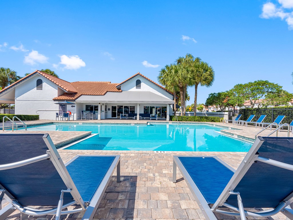 A pool with sun loungers in front of a white building with a red roof.